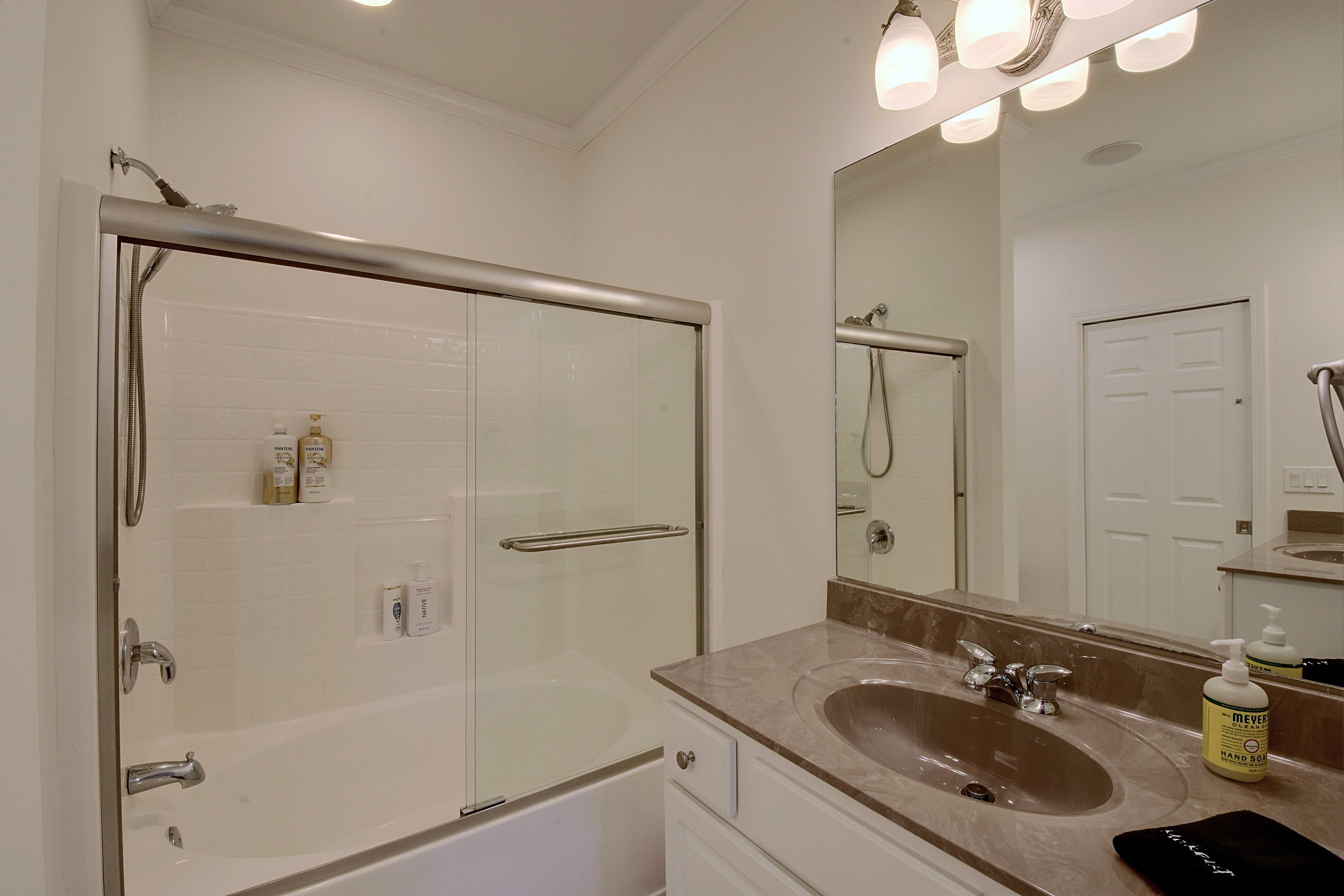 Primary bathroom with vanity, mirror, and tub/shower combination with sliding glass doors.