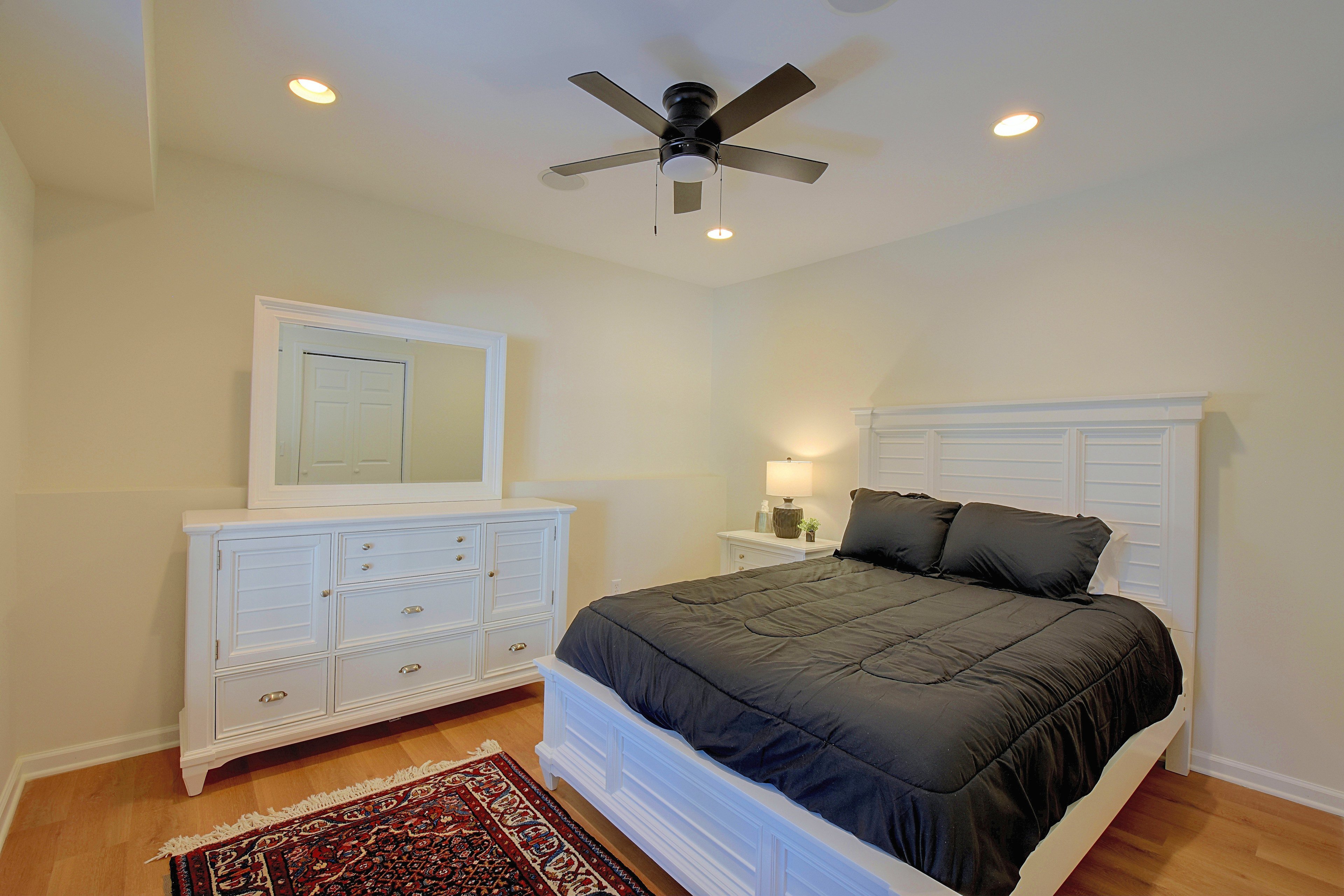 Second bedroom featuring a queen bed with white headboard, dresser with mirror, and area rug.