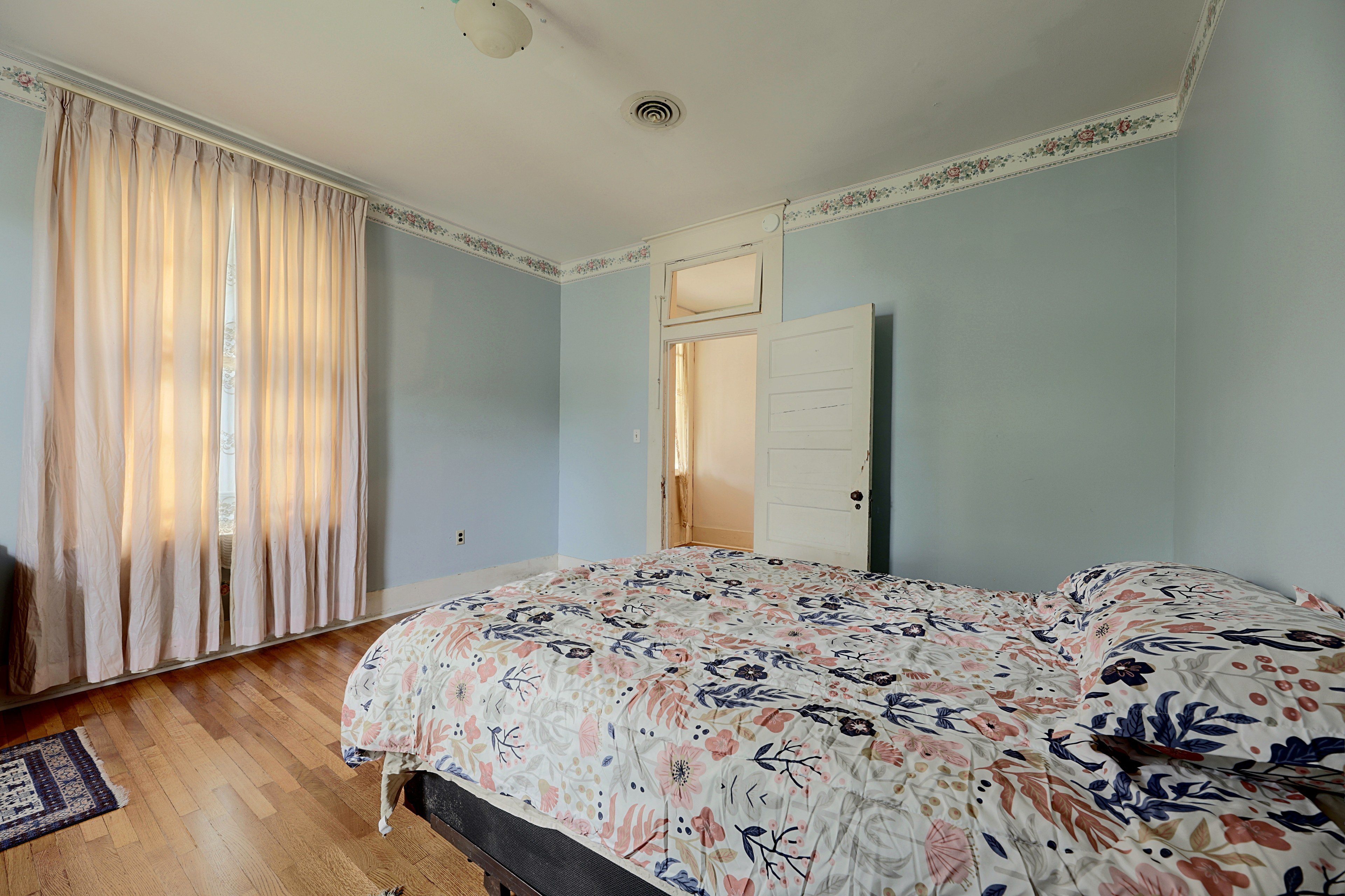 Additional view of the blue bedroom with draped window treatment and rug.