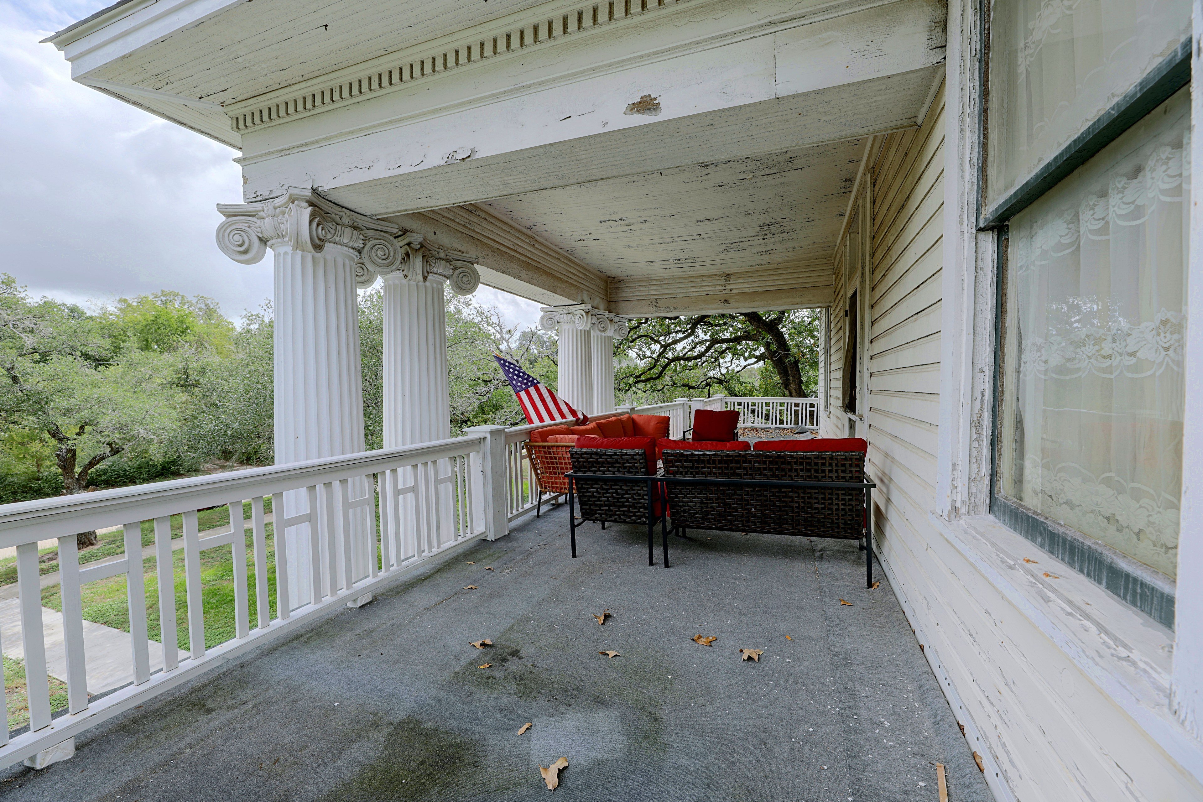 Second-story covered porch with seating, classic columns, and tree views.