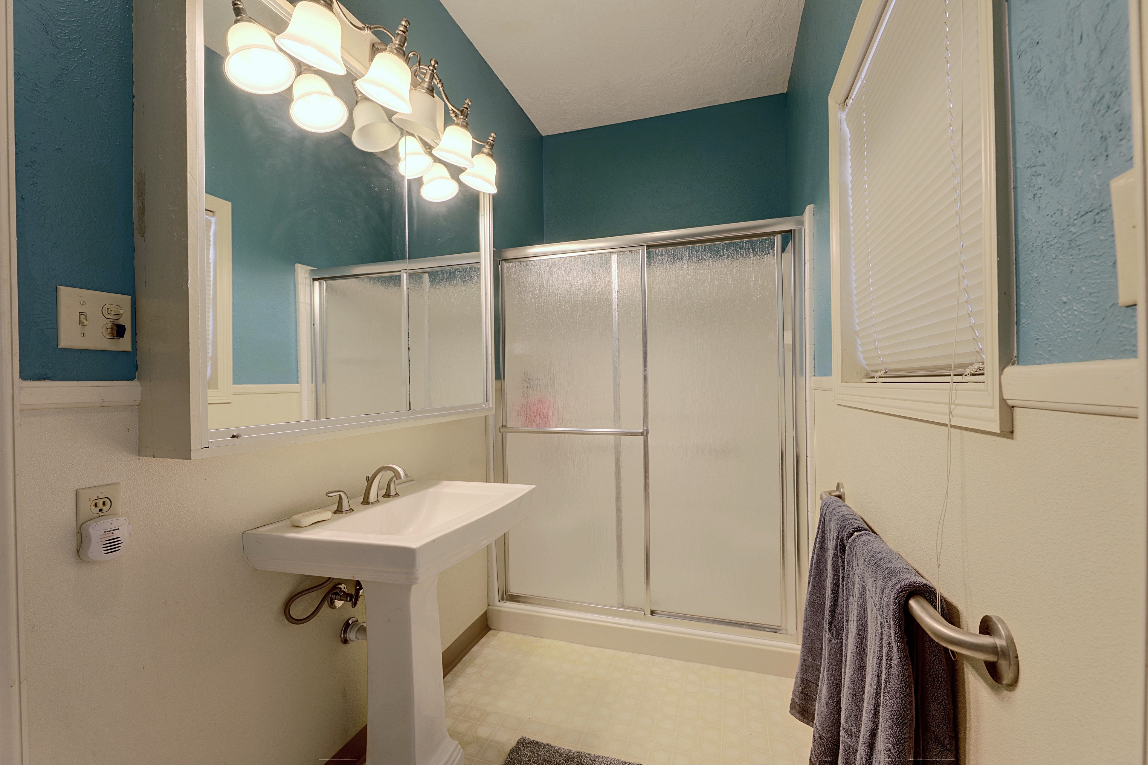 Bathroom with deep teal walls, white wainscoting, pedestal sink, and walk-in shower.