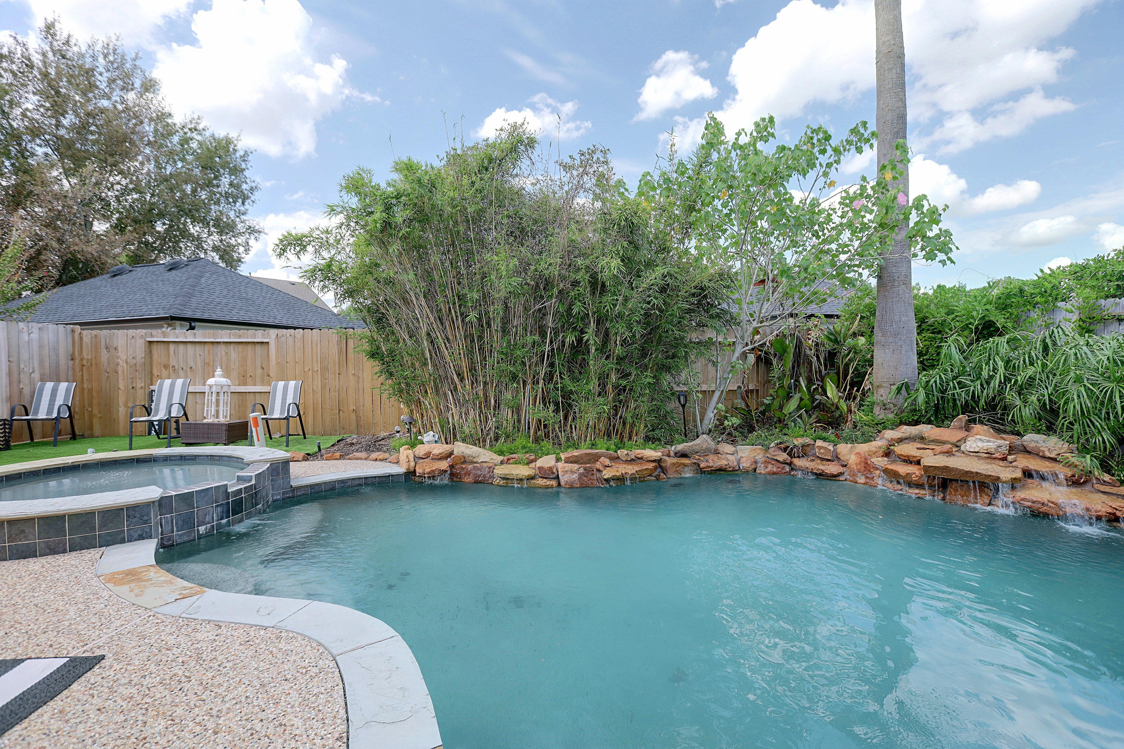Private backyard featuring in-ground pool, overflowing spa, and rock waterfall
